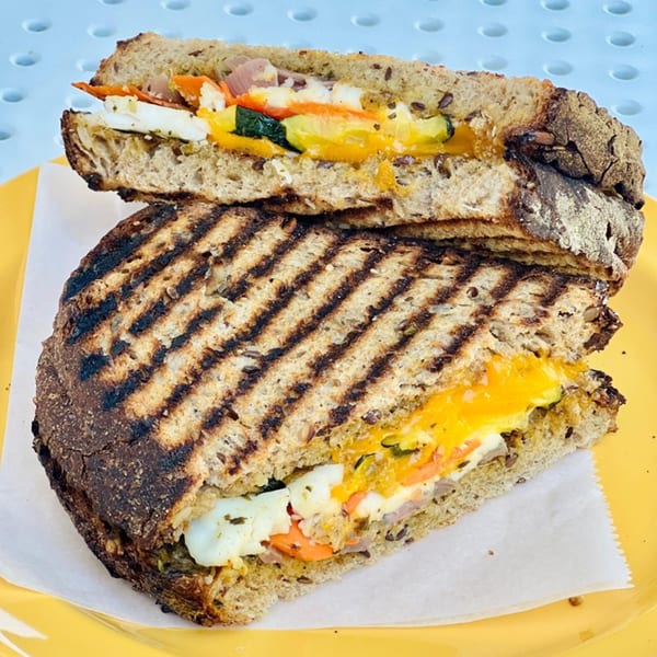 Grilled panini sandwich cut in half, revealing melted cheese, vegetables, and egg on a yellow plate.