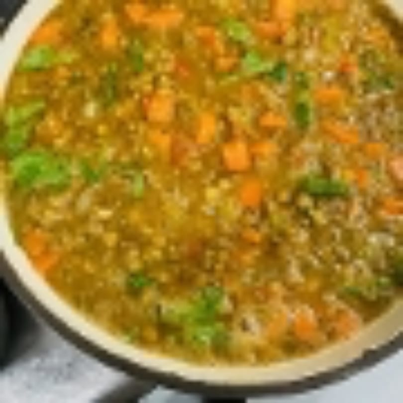 Hearty lentil soup with diced carrots and fresh green herbs in a white bowl.